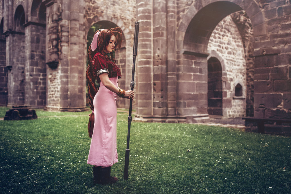 cosplayer in a church ruin wearing a pink dress and auburn wig with a long braid and large bangs